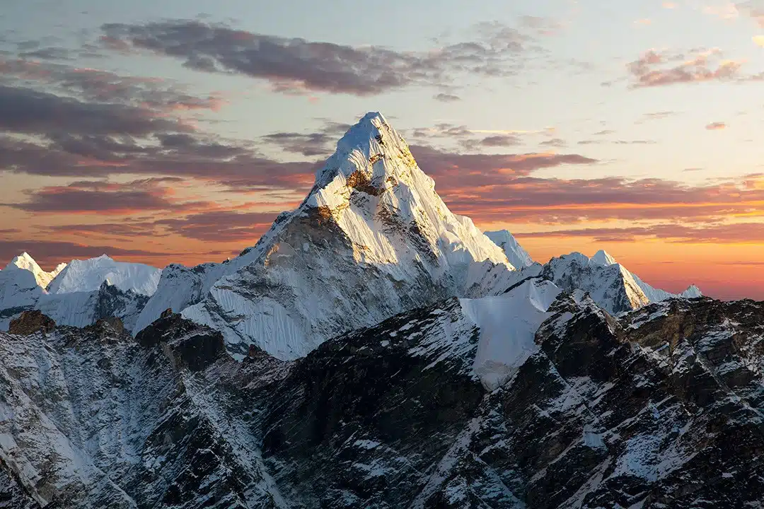 Snowy alpine peak bathed in sunset light over rugged, shadowed ridges