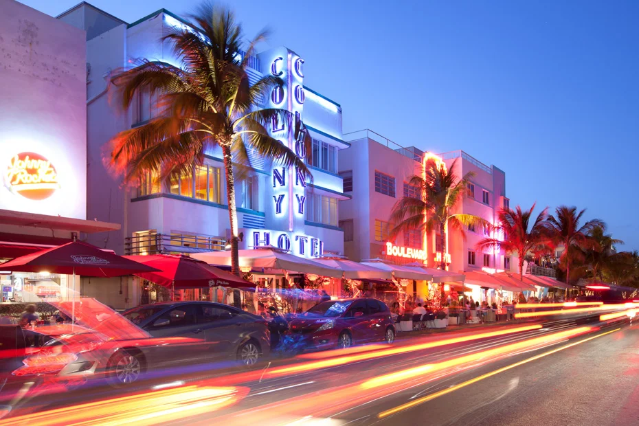 Miami Beach neon-lit hotel street with palm trees and diners at night