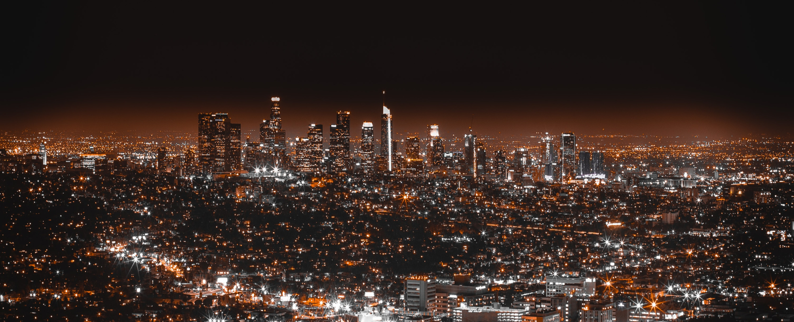 Nighttime city skyline with illuminated skyscrapers and sprawling urban lights.