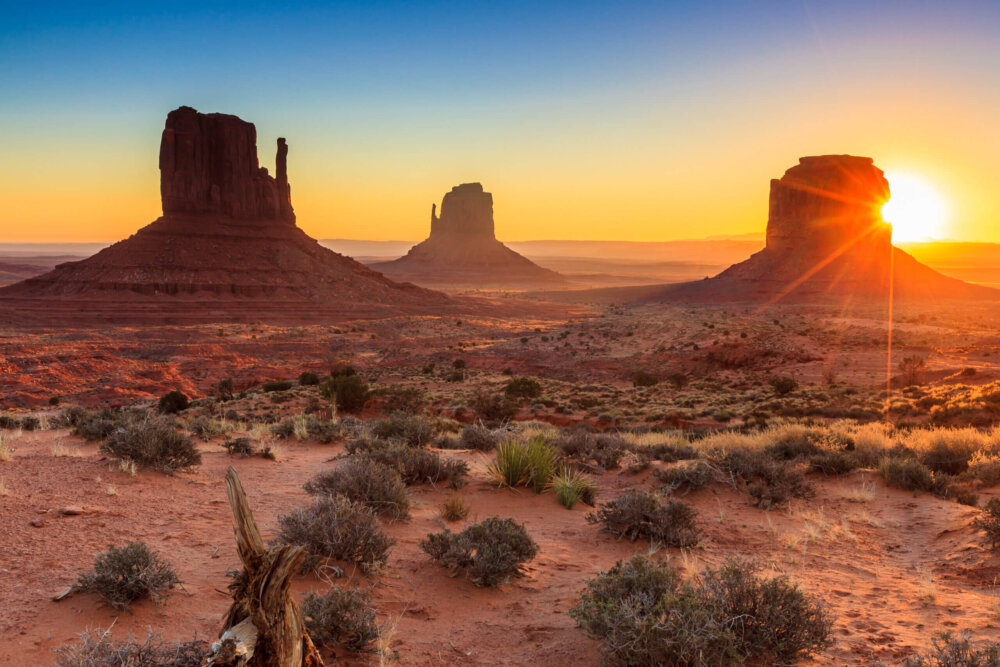 Monument Valley rock formations at sunset with a sunburst over the desert