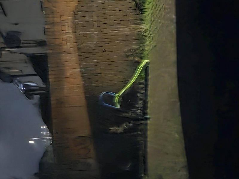 Discarded neon-accented crutch leans against a weathered brick pillar at night near a parked car