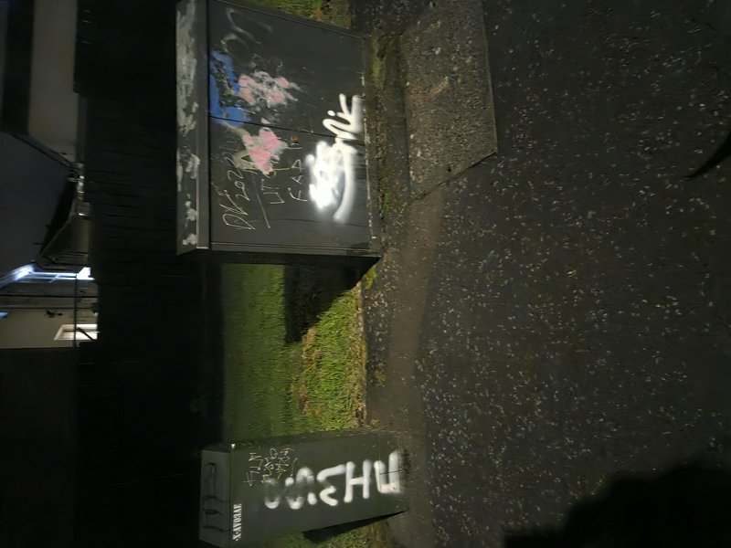 Spray-painted graffiti covers dark utility boxes beside a residential sidewalk at night