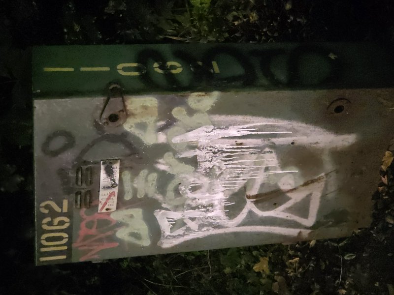 Layered graffiti covers an old weathered metal street sign resting on grass at night
