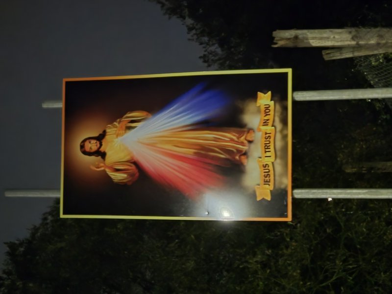 Outdoor Divine Mercy Jesus sign mounted on a fence at dark, displaying Jesus I Trust In You text