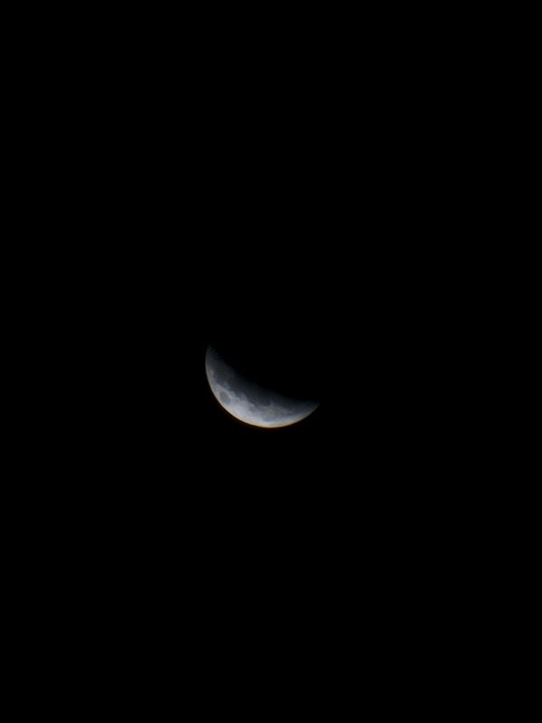 Delicate pale crescent moon with faint earthshine centered against a completely empty pitch black...