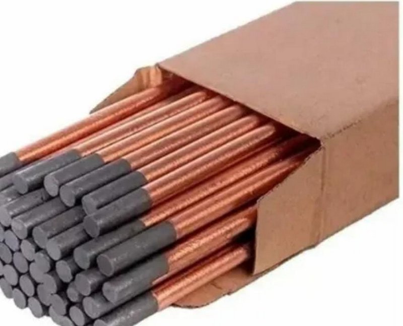 Open cardboard box holding stacked copper-coated carbon arc gouging electrodes against a plain wh...