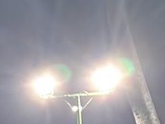 Low angle view of a glowing dual-head street lamp with lens flare against a hazy dusk sky
