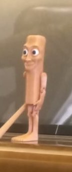 Uncanny tall flesh-toned cartoon figurine with big googly eyes stands on a glass display shelf