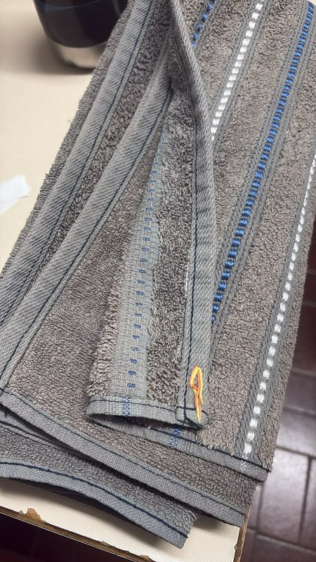 Folded gray terry cloth towel with decorative stitched trim rests on a light countertop
