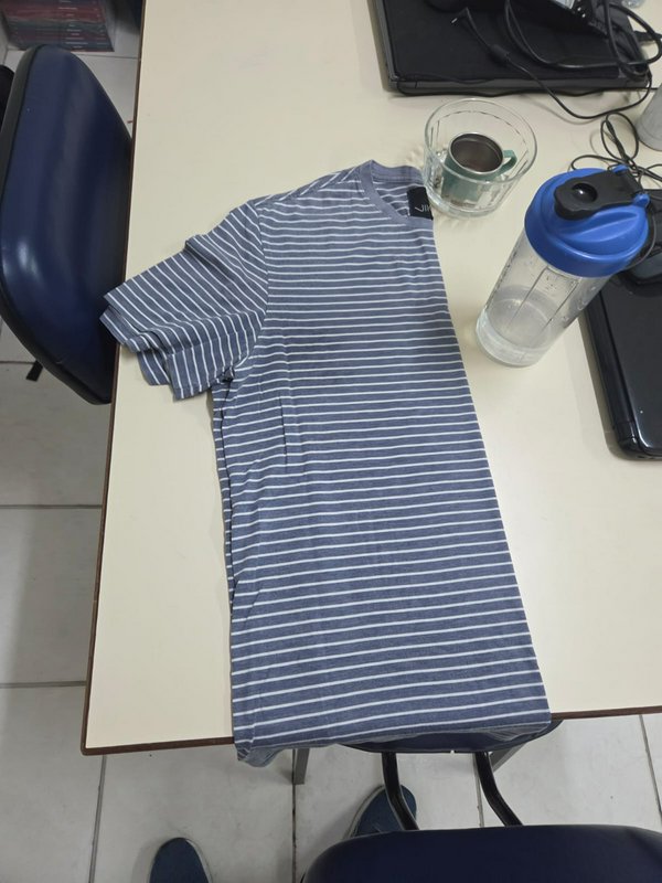 Folded blue and white horizontal striped t-shirt laid flat on a light office desk next to drinkware