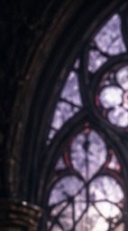 Blurred close-up of Gothic church stained glass, showing dark lead tracery framing soft purple ti...