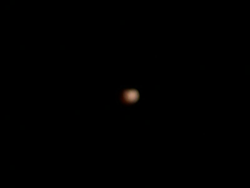Blurred out-of-focus reddish blood moon lunar eclipse glowing faintly against a completely pitch ...