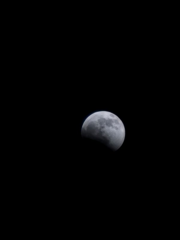 Partial lunar eclipse of a pale grey moon hanging against a pitch black empty night sky