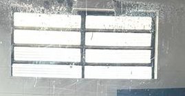 Looking through a smudged grimy grid-paned security window at bright overexposed exterior light