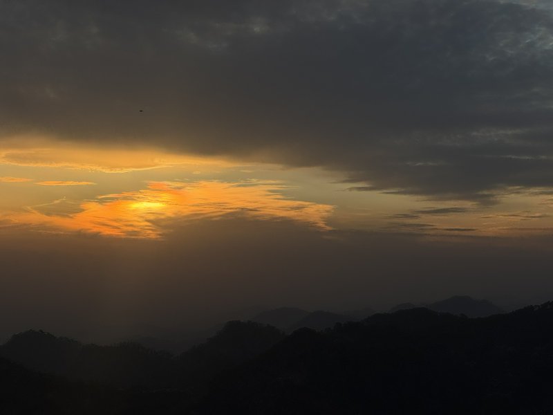 Golden sunset glows through dark storm clouds above silhouetted layered mountain peaks