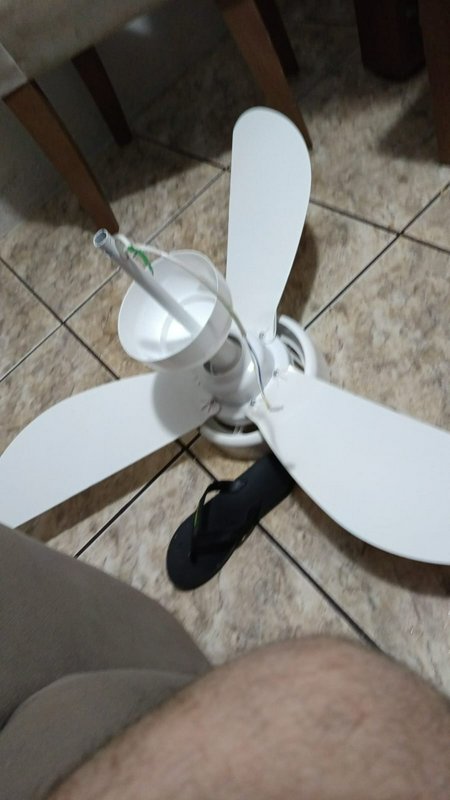 Disassembled white 3-blade ceiling fan resting on beige tiled home floor next to a flip flop duri...