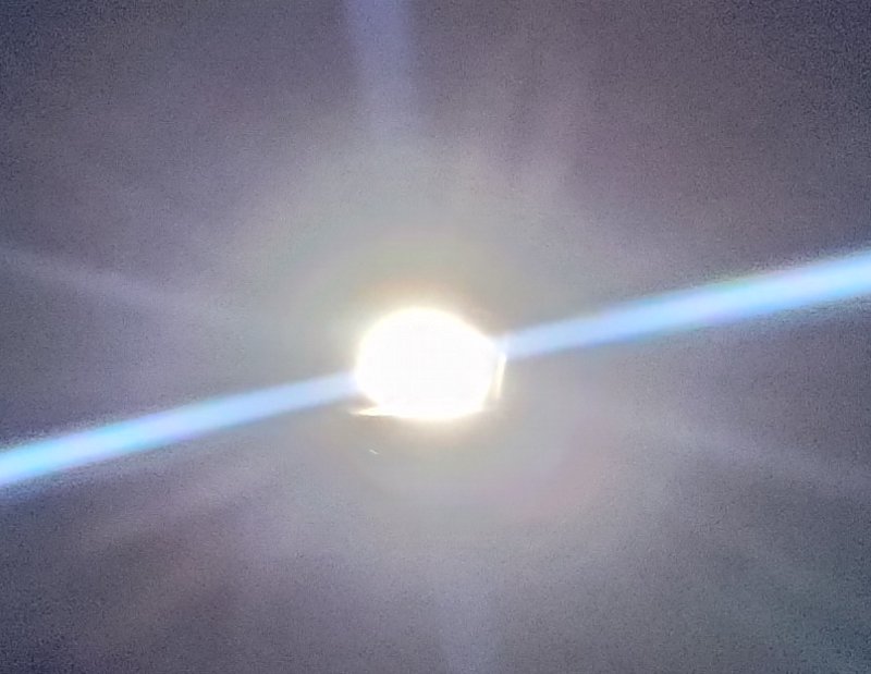 Intensely bright round glowing light source with diagonal blue lens flare streaks against a soft ...