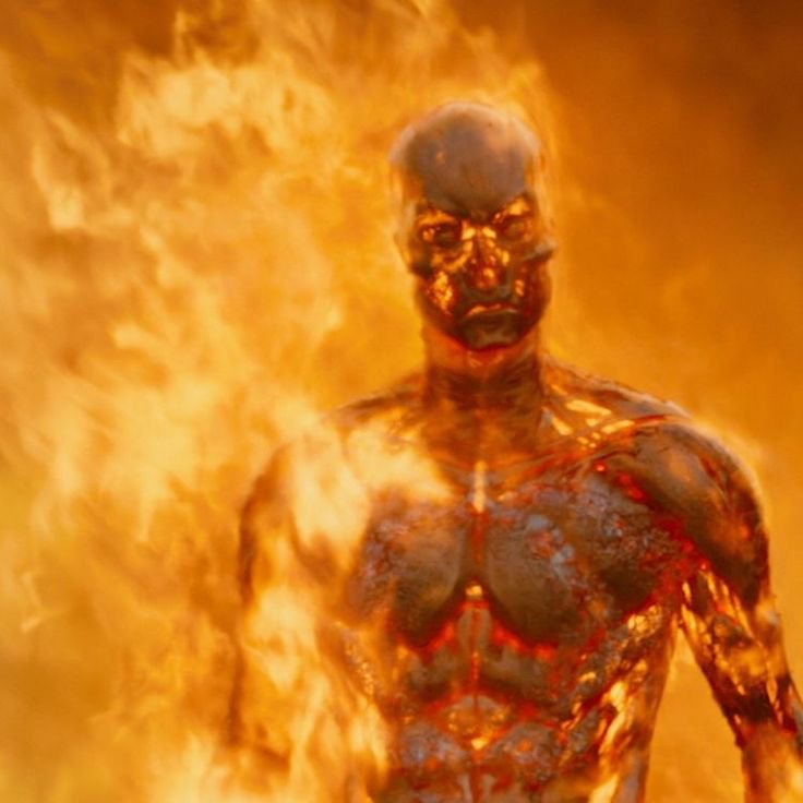 Muscular molten metallic humanoid figure standing amid roaring bright orange flames