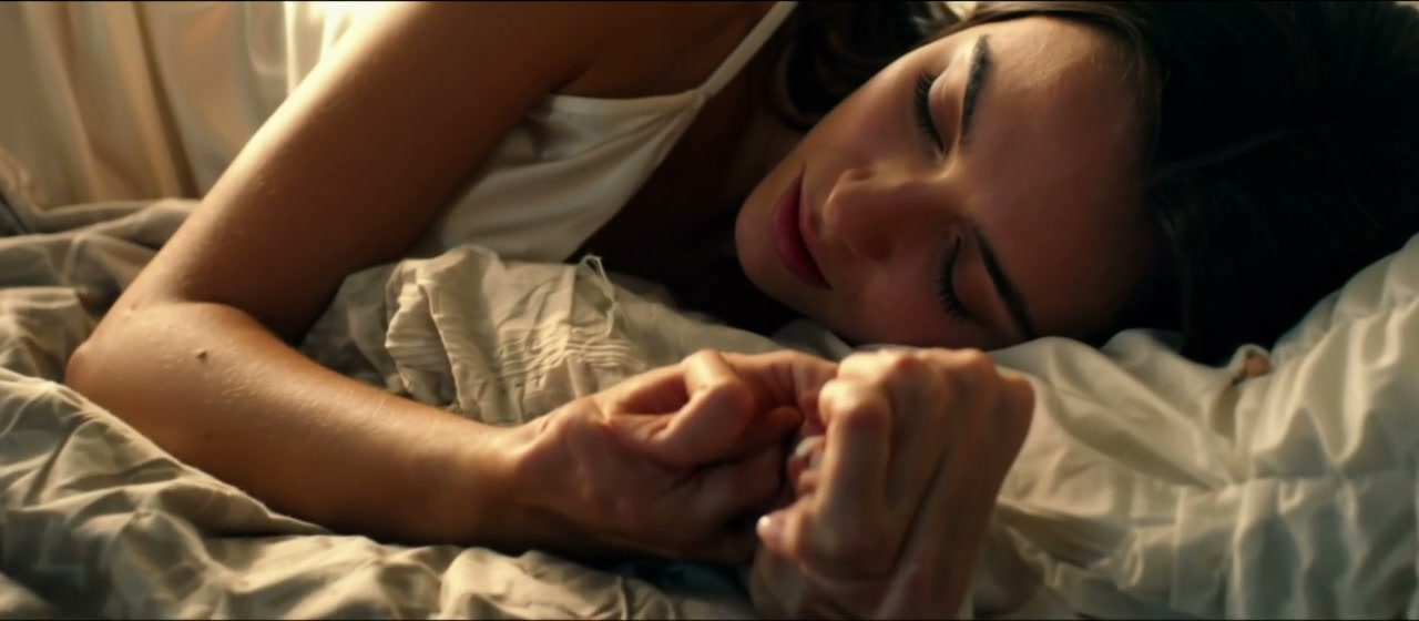 Close-up of peaceful woman lying in bed, eyes closed, smiling while clasping a partner's hands in...