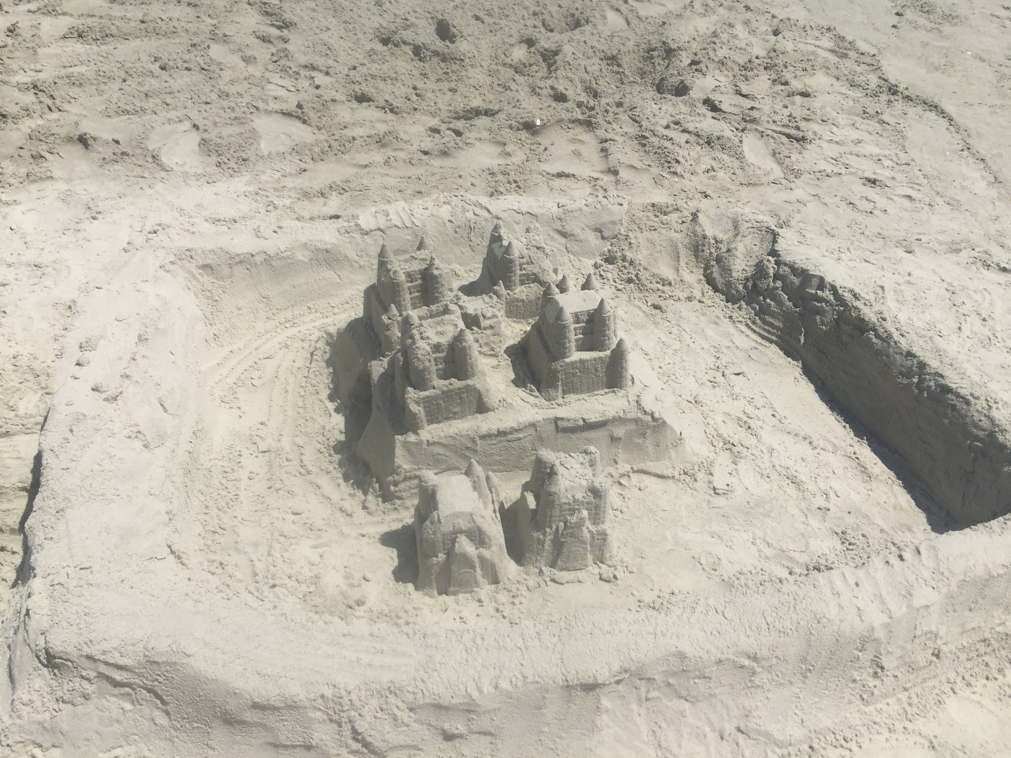 Intricate multi-towered sand castle sits inside a dug sand moat on a sunlit sandy beach