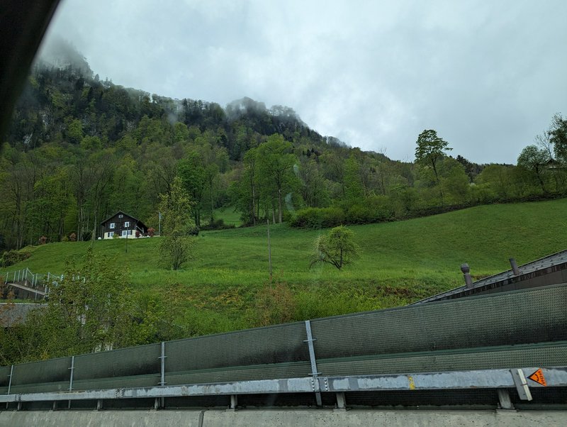 Misty forested alpine hillside with a traditional chalet viewed from a highway on an overcast day