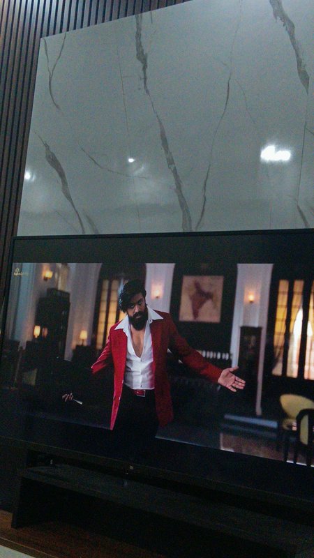 Wall mounted smart TV displaying KGF movie scene with actor Yash, set below a grey marble feature...