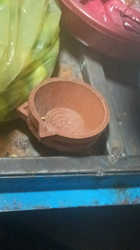 Unfired handcrafted terracotta diya with engraved sun motif rests on a metal work tray
