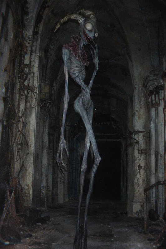 Tall gaunt horned skeletal monster stands in a decaying dark arched stone corridor