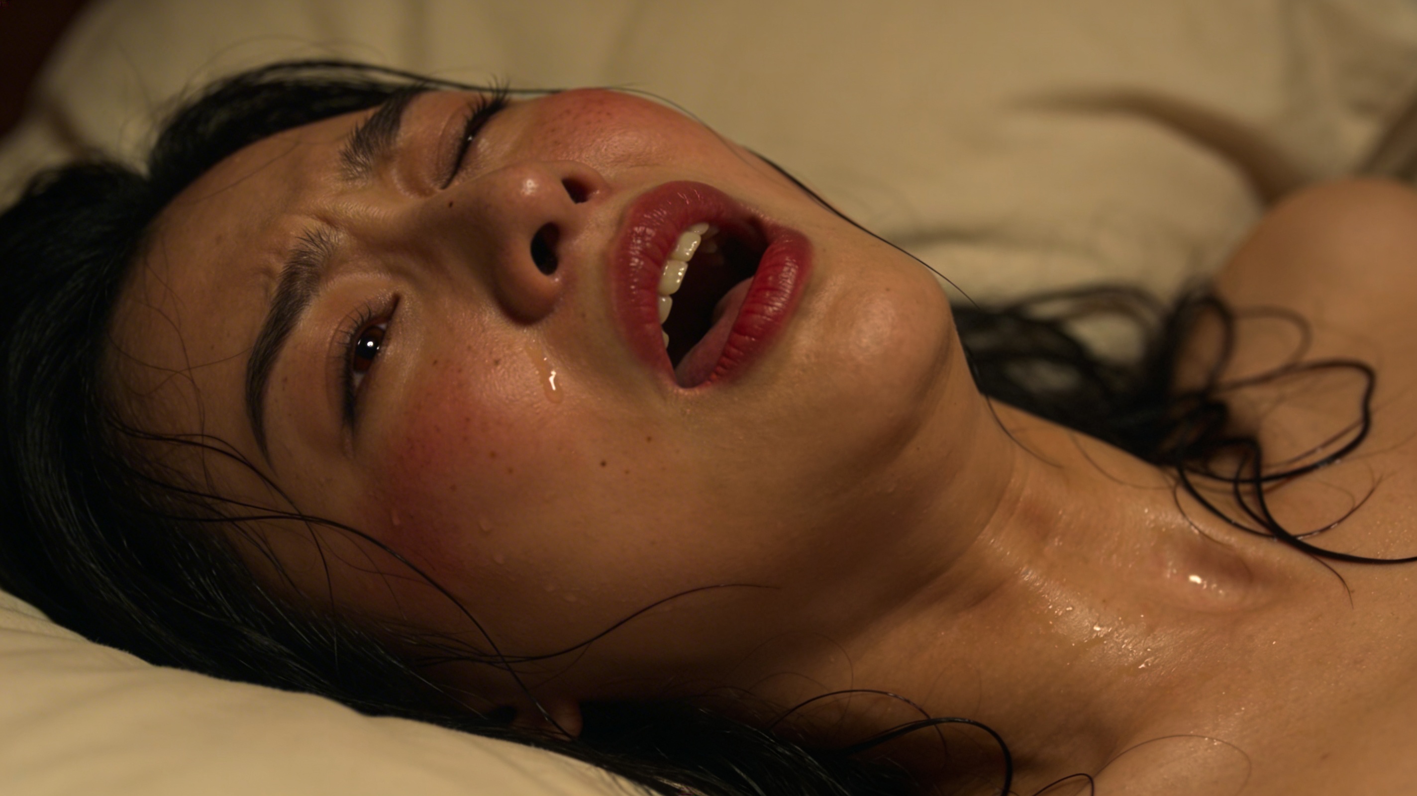 Close-up of a woman lying on a pillow with mouth open and red lipstick.