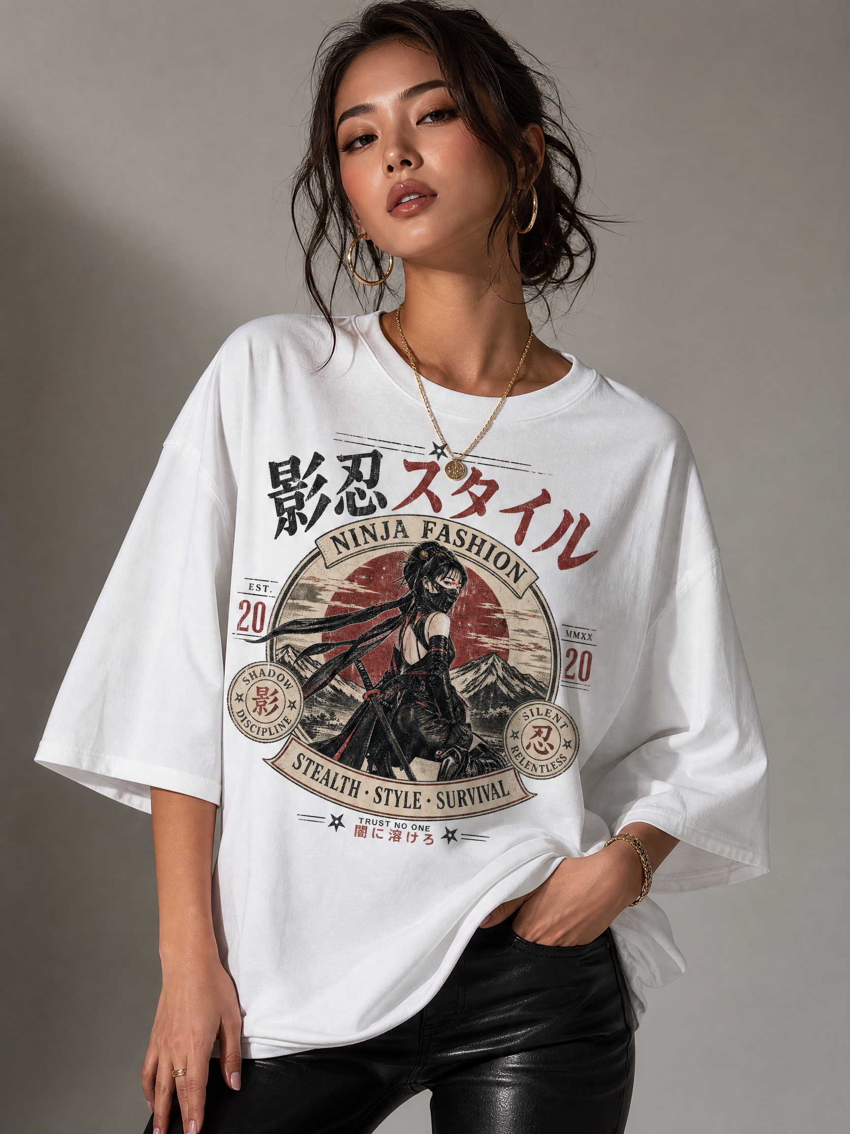 Woman in an oversized white graphic tee with Ninja Fashion design and red sun motif, wearing gold jewelry.