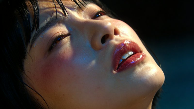 Close-up of a woman's face tilted upward with glossy red lips and dewy skin.