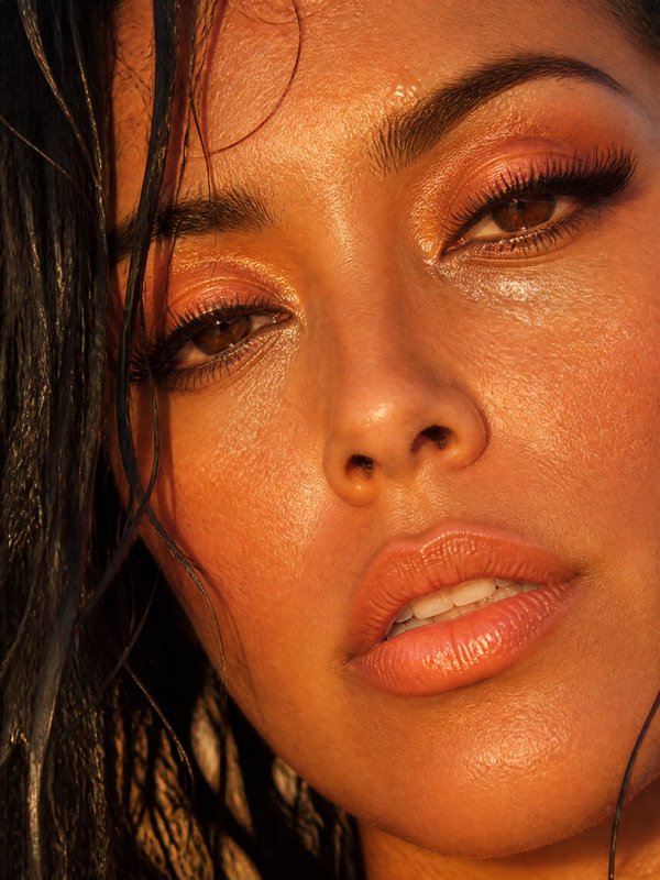 Close-up of a woman with sun-kissed, dewy skin and bronze makeup.