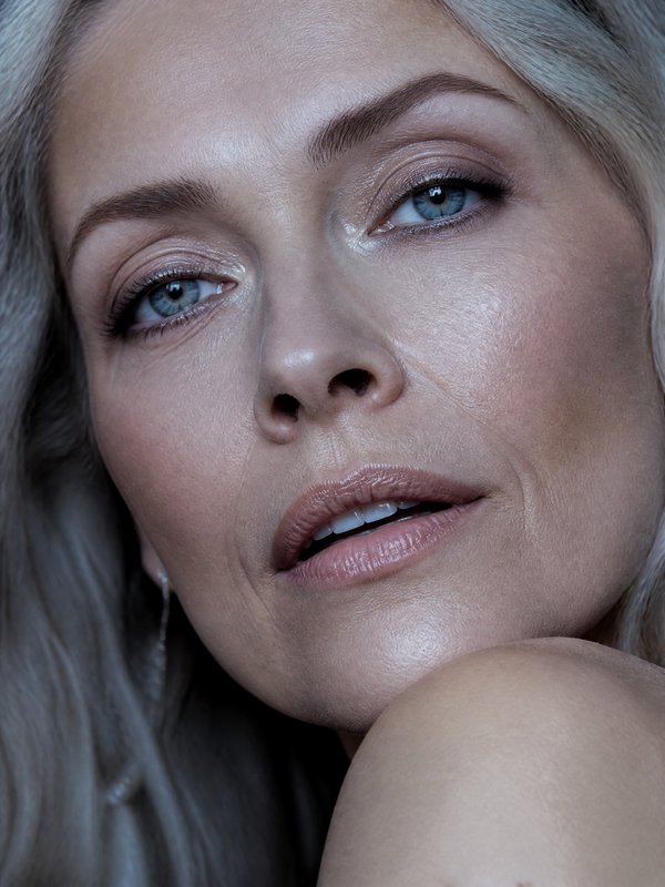 Close-up portrait of a woman with blue eyes, nude makeup, and smooth skin.
