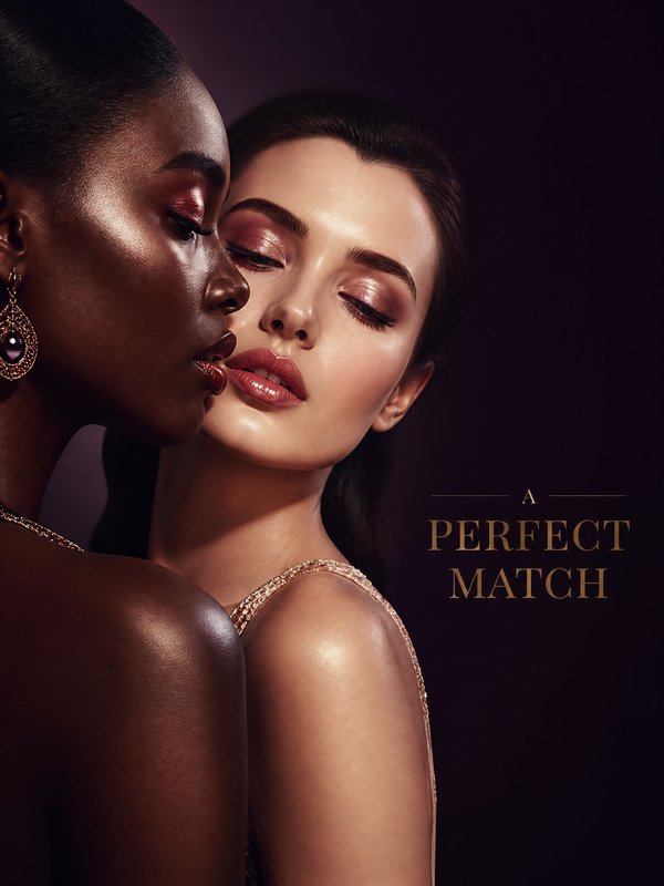 Two glamorous women in a close-up pose with metallic makeup and jewelry, against a dark backdrop.