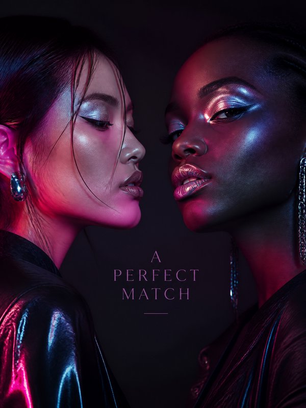 Two women facing each other under neon pink and blue lighting with metallic makeup.