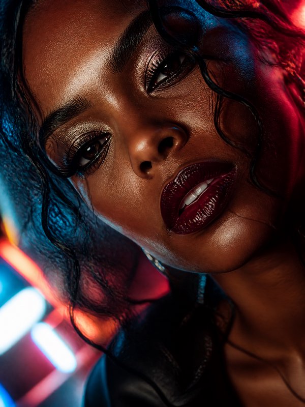 Close-up portrait of a woman with glossy burgundy lips under blue and red neon lighting.