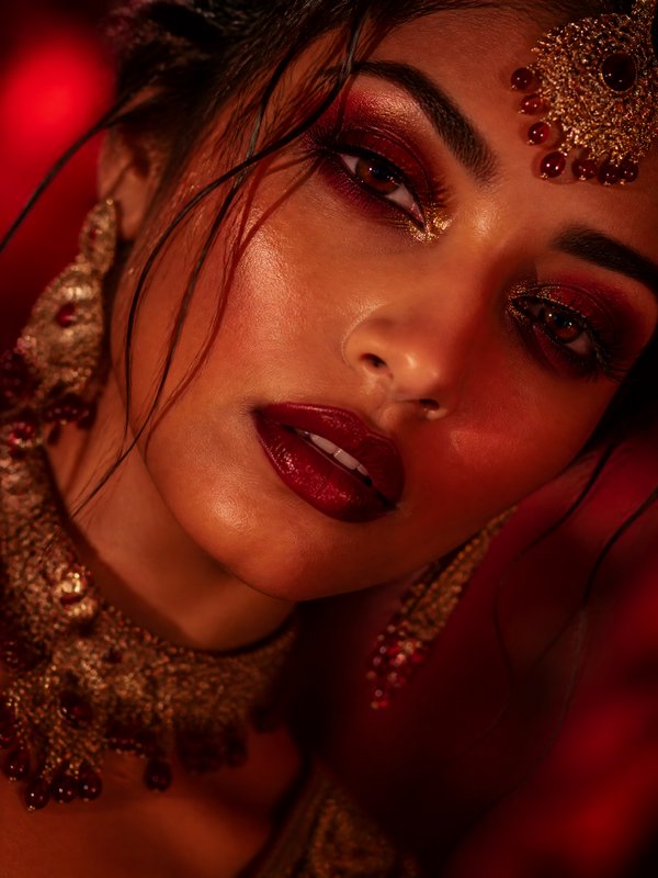 Close-up of a woman wearing gold jewelry and bold red makeup with a jeweled headpiece.