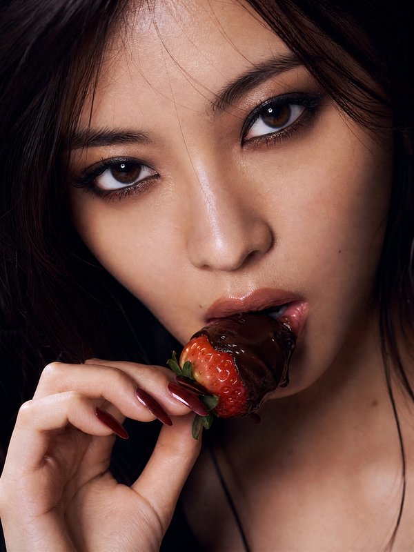 Close-up of a woman biting a chocolate-dipped strawberry with glossy lips.