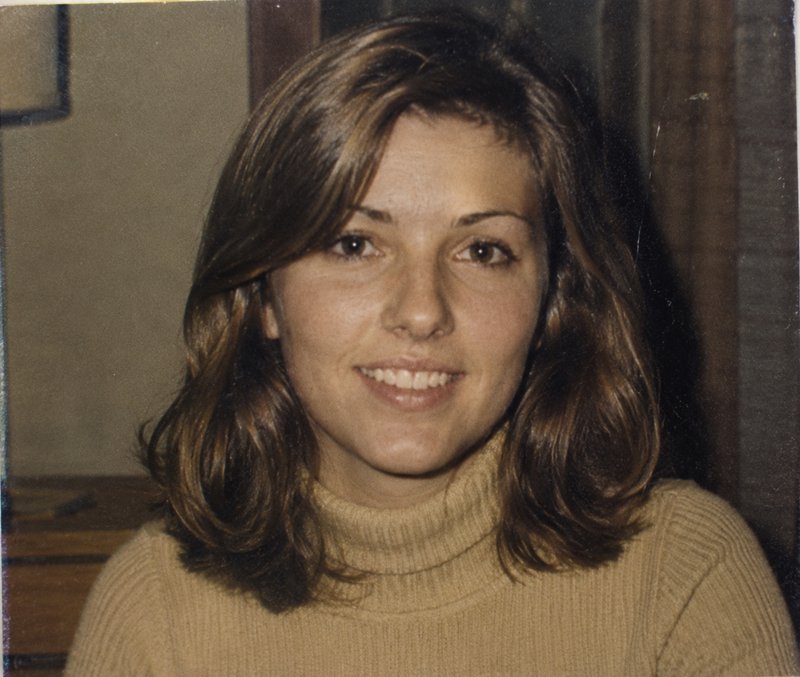 Woman with shoulder-length brown hair in a beige turtleneck sweater smiling.