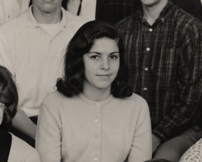 Woman with dark wavy hair in a light cardigan, seated in a vintage black-and-white group portrait.