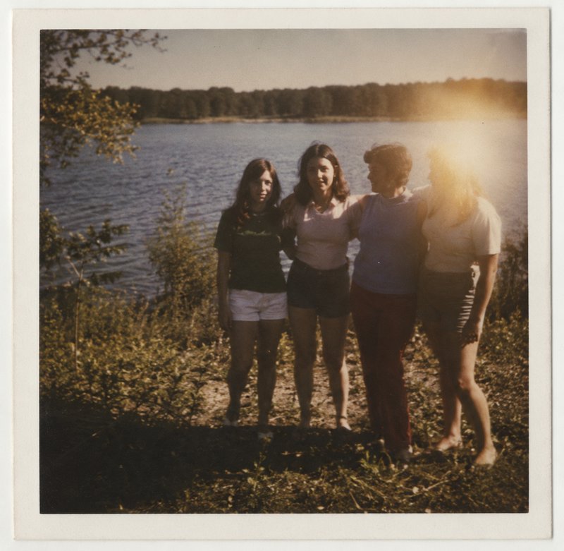 Four friends standing by a lake at sunset with a warm glow.