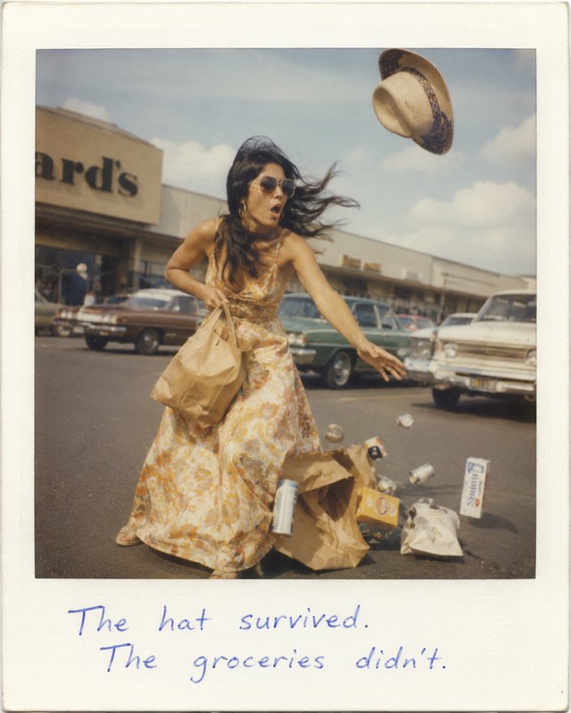 Woman in a floral dress in a parking lot as groceries spill and a hat flies away.