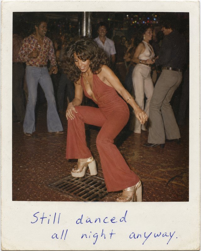 Woman in a rust jumpsuit dancing on a crowded retro dance floor with platform heels.