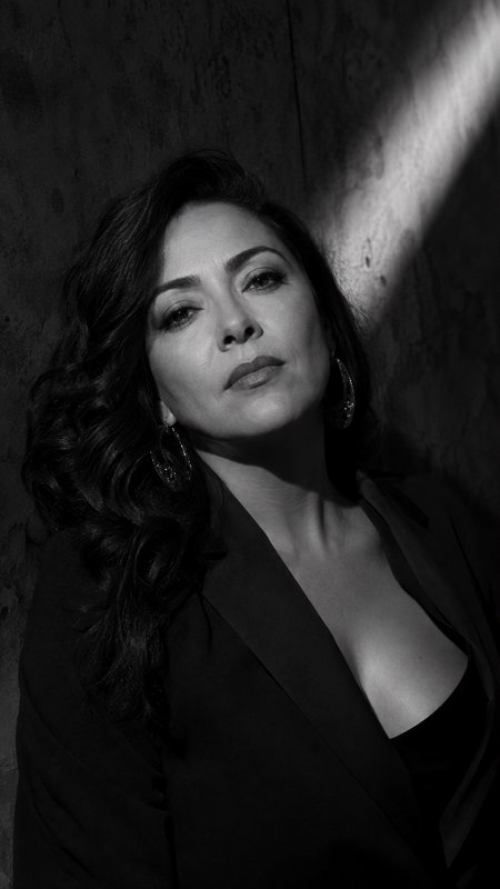 [High contrast black and white portrait of an elegant woman with wavy dark hair, dramatic diagonal lighting, and large hoo...
