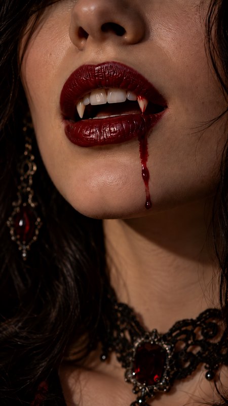 Close-up of a vampire's sharp fangs, with blood dripping from glossy deep red lips