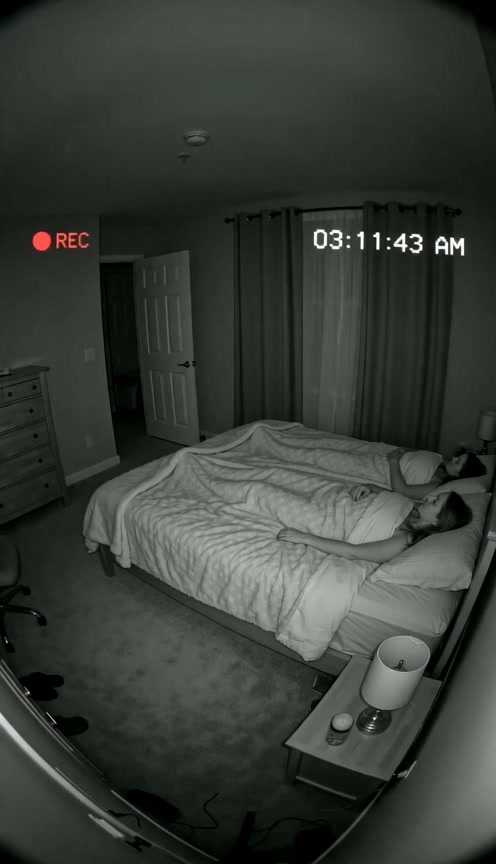 Night vision security camera footage of a couple sleeping in a bedroom, timestamped 3:11 AM with ...