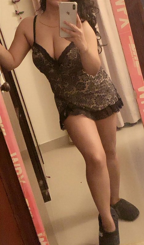 Woman taking a full length mirror selfie wearing a black lace chemise nightgown and fuzzy house s...