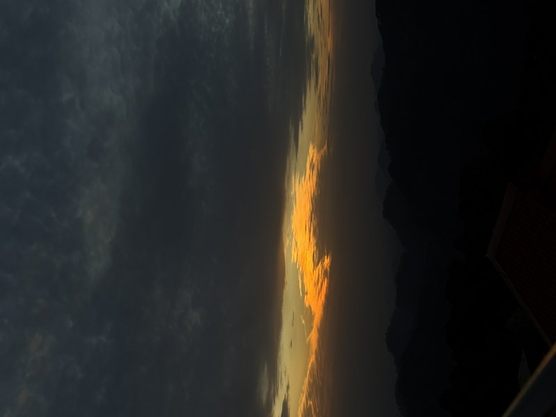 Fiery orange sunlit clouds contrast against a dark stormy dusk sky with silhouetted landscape edge
