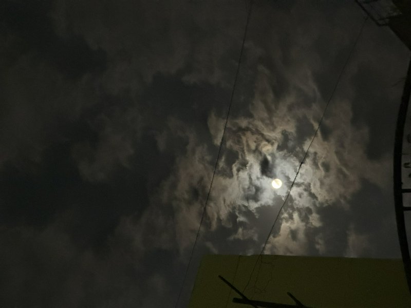 Glowing full moon peeks through swirling wispy clouds over an urban night sky