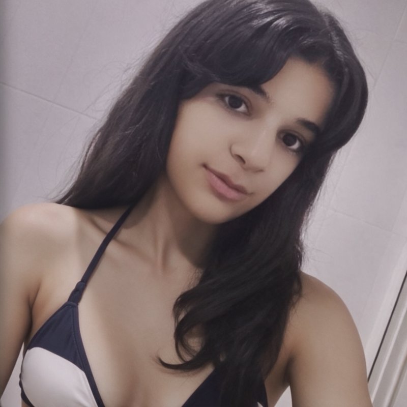 Close-up casual selfie of young woman with long dark wavy hair, soft smile, wearing black and whi...